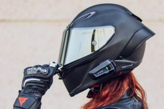 Gros plan d'un casque intégral noir en carbone avec écran iridium et intercom Cardo, ajusté à la main avec un gant