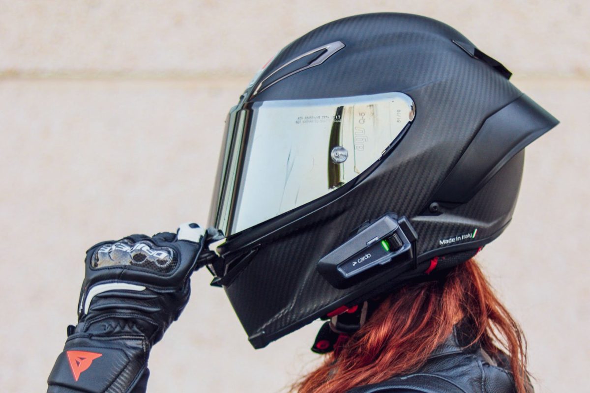 Gros plan d'un casque intégral noir en carbone avec écran iridium et intercom Cardo, ajusté à la main avec un gant